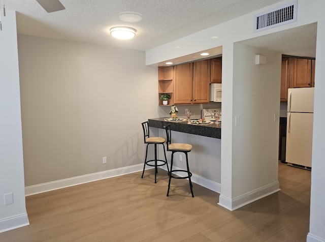 kitchen featuring visible vents, a kitchen breakfast bar, white appliances, light wood-style floors, and brown cabinetry