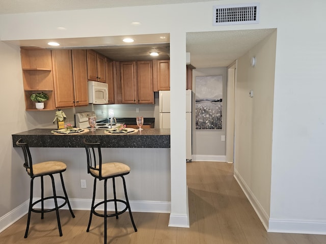 kitchen with dark countertops, visible vents, a peninsula, white appliances, and open shelves