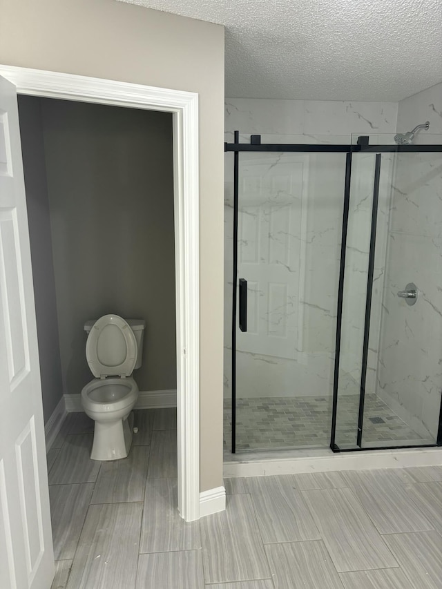 bathroom featuring a textured ceiling, a marble finish shower, toilet, and baseboards