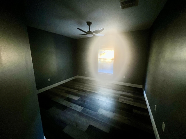 empty room featuring baseboards, dark wood-type flooring, visible vents, and a ceiling fan