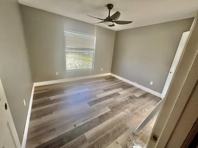 unfurnished room with a textured ceiling, wood finished floors, a ceiling fan, and baseboards