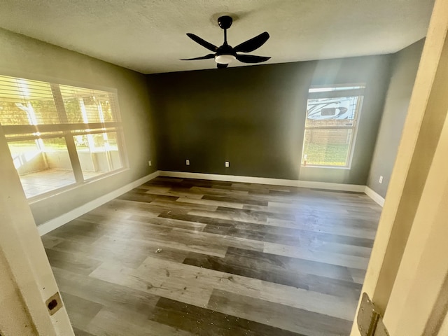 spare room with a textured ceiling, baseboards, dark wood finished floors, and a ceiling fan