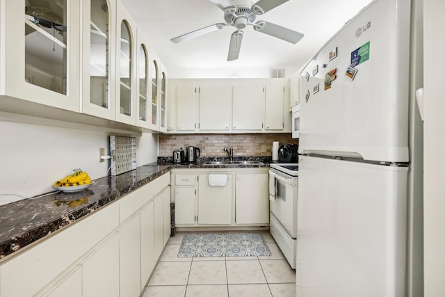 kitchen featuring white cabinetry, backsplash, dark stone counters, light tile patterned floors, and white appliances