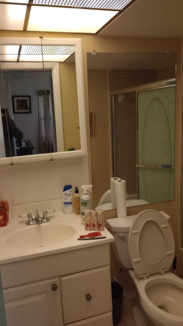 bathroom with toilet, decorative backsplash, walk in shower, and vanity