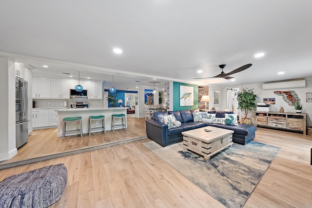 living room with ceiling fan, light hardwood / wood-style flooring, and a wall unit AC