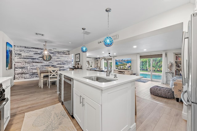 kitchen featuring pendant lighting, white cabinetry, sink, light wood-type flooring, and a center island with sink