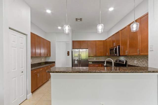 kitchen featuring appliances with stainless steel finishes, kitchen peninsula, dark stone countertops, and decorative light fixtures