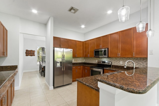 kitchen with dark stone countertops, appliances with stainless steel finishes, hanging light fixtures, and kitchen peninsula