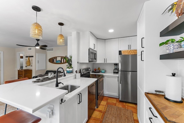 kitchen with hanging light fixtures, sink, kitchen peninsula, white cabinetry, and appliances with stainless steel finishes