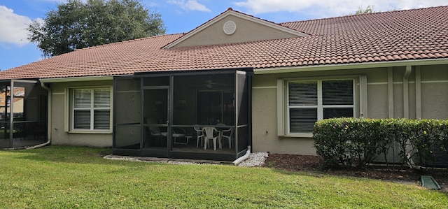 rear view of house featuring stucco siding, a sunroom, a tiled roof, and a lawn