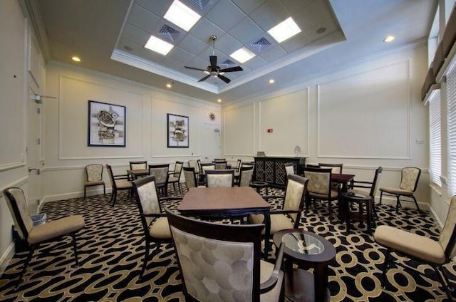 carpeted dining area with a decorative wall, visible vents, crown molding, ceiling fan, and a raised ceiling