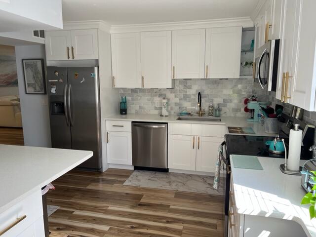 kitchen with sink, tasteful backsplash, dark hardwood / wood-style flooring, stainless steel appliances, and white cabinets