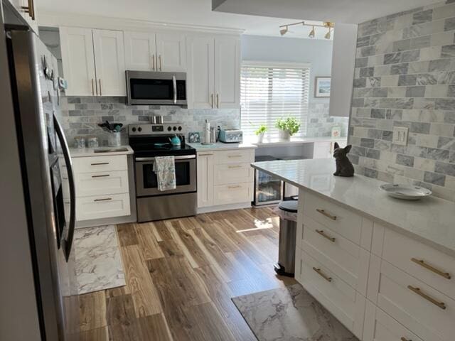 kitchen with stainless steel appliances, white cabinets, and light hardwood / wood-style flooring