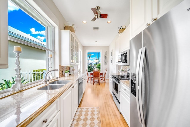 kitchen featuring pendant lighting, light stone counters, sink, white cabinetry, and stainless steel appliances