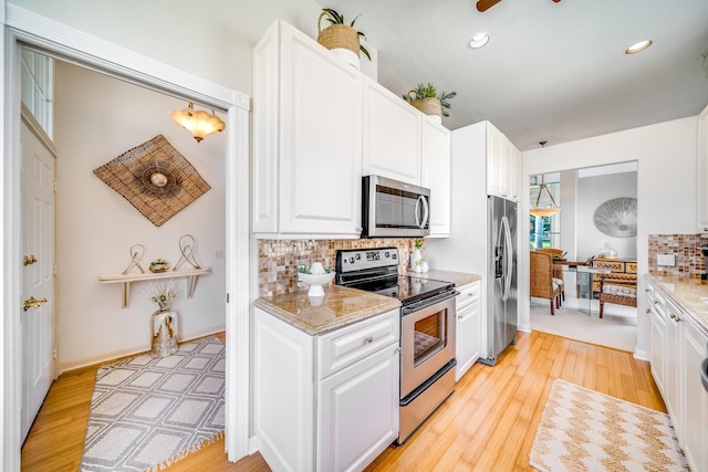 kitchen with light stone counters, white cabinets, light hardwood / wood-style flooring, stainless steel appliances, and decorative backsplash