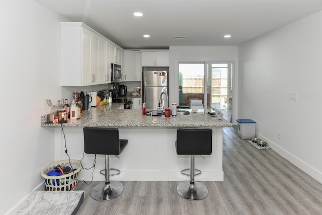 kitchen with kitchen peninsula, a kitchen bar, stainless steel appliances, and white cabinets