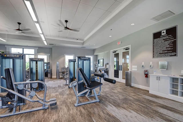 exercise room featuring a raised ceiling, hardwood / wood-style floors, ceiling fan, and french doors