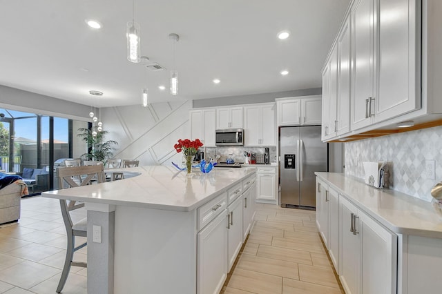 kitchen with appliances with stainless steel finishes, hanging light fixtures, white cabinetry, and a large island