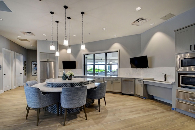 kitchen with appliances with stainless steel finishes, gray cabinetry, a breakfast bar area, light wood-type flooring, and decorative light fixtures