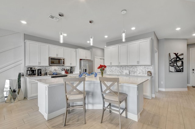 kitchen with appliances with stainless steel finishes, a center island with sink, and white cabinets