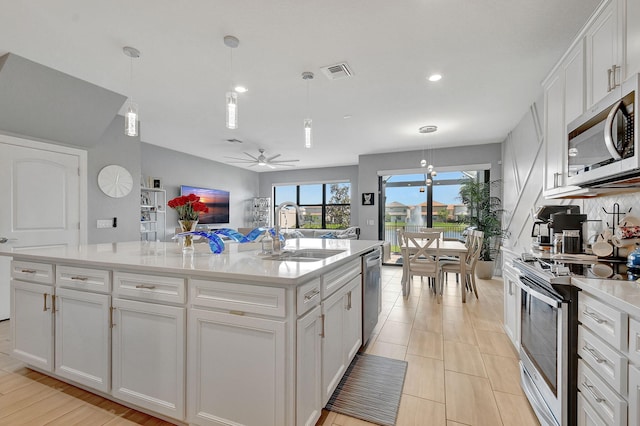 kitchen with appliances with stainless steel finishes, hanging light fixtures, white cabinets, a center island with sink, and sink