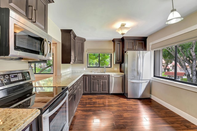 kitchen featuring pendant lighting, light stone counters, stainless steel appliances, dark brown cabinetry, and dark hardwood / wood-style flooring