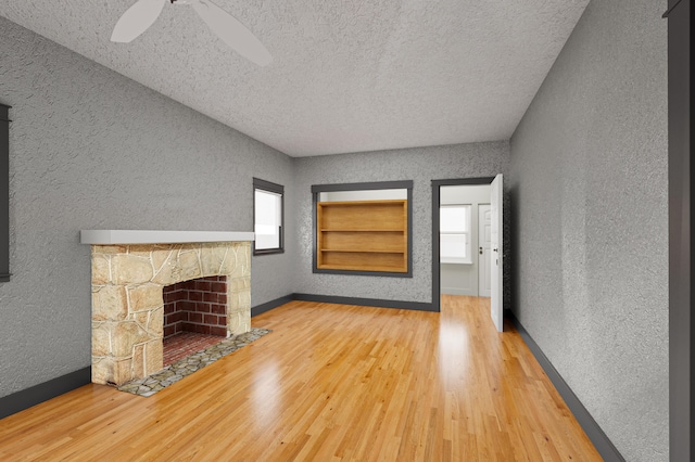 unfurnished living room featuring hardwood / wood-style flooring, a textured ceiling, built in features, and a stone fireplace