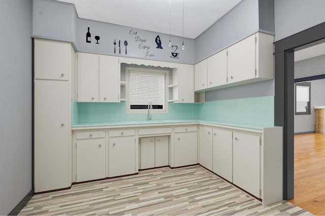 kitchen featuring tasteful backsplash, light wood-type flooring, sink, and white cabinetry