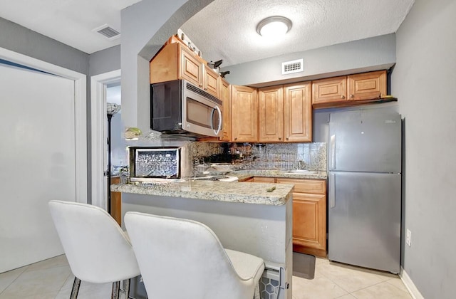 kitchen with a breakfast bar area, stainless steel appliances, decorative backsplash, light tile patterned flooring, and light stone countertops