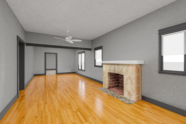 unfurnished living room featuring ceiling fan, hardwood / wood-style floors, a textured ceiling, and a stone fireplace