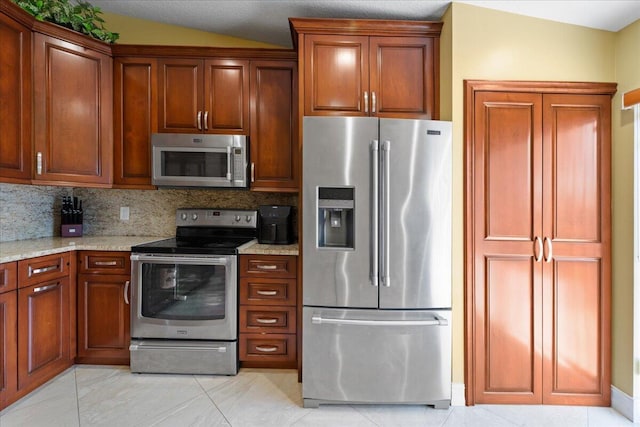 kitchen with light stone counters, light tile patterned flooring, vaulted ceiling, stainless steel appliances, and backsplash