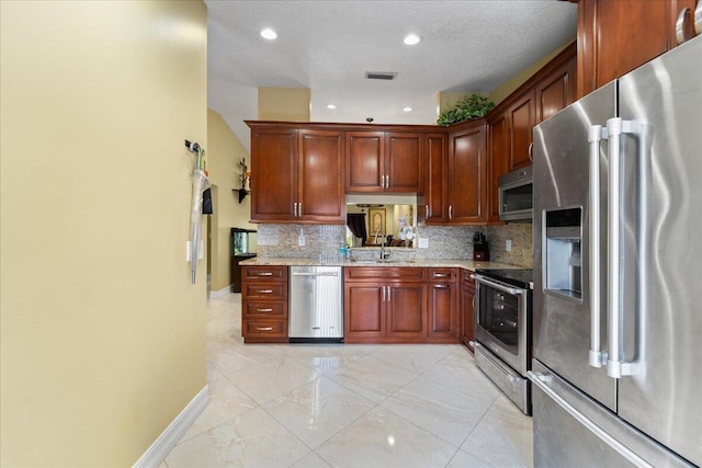 kitchen with sink, a textured ceiling, appliances with stainless steel finishes, light stone countertops, and decorative backsplash