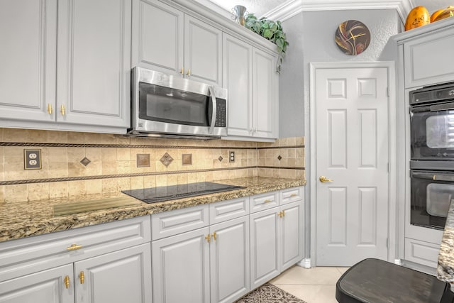 kitchen with white cabinetry, ornamental molding, light tile patterned flooring, black appliances, and stone counters