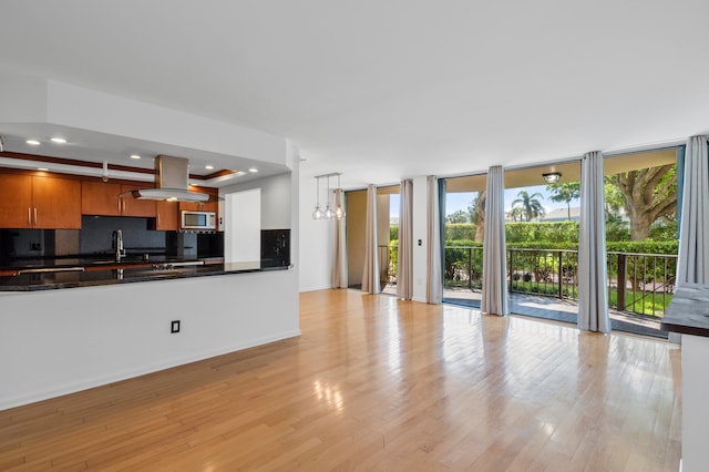 kitchen featuring pendant lighting, sink, stainless steel microwave, light hardwood / wood-style floors, and decorative backsplash