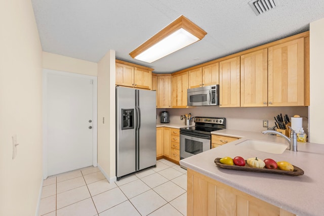 kitchen with light brown cabinets, light tile patterned floors, stainless steel appliances, and sink