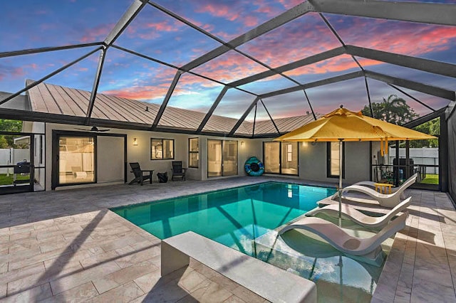 pool at dusk featuring a patio area, glass enclosure, and ceiling fan