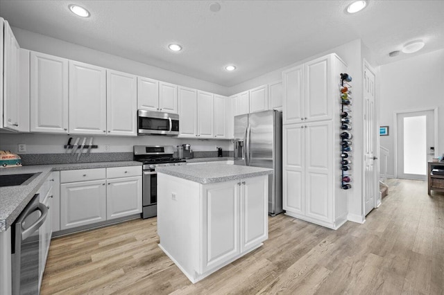 kitchen featuring appliances with stainless steel finishes, a kitchen island, white cabinetry, and light hardwood / wood-style flooring