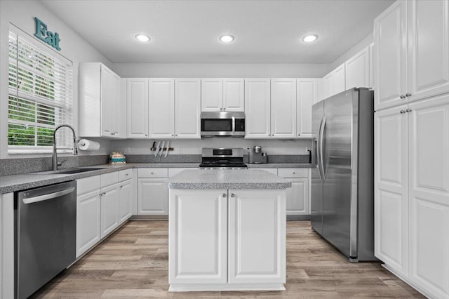 kitchen with light hardwood / wood-style floors, sink, white cabinets, appliances with stainless steel finishes, and a center island