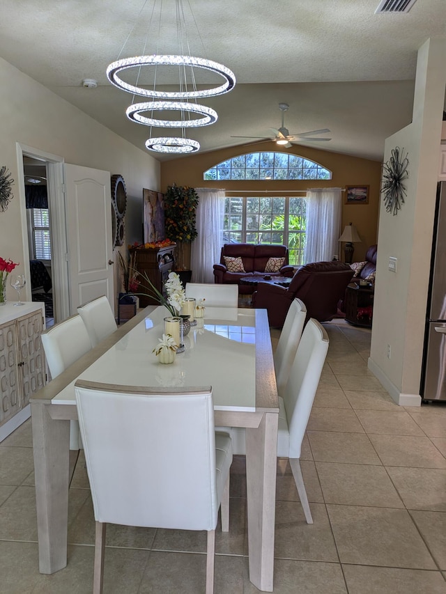 dining room featuring ceiling fan with notable chandelier, light tile patterned flooring, lofted ceiling, and a textured ceiling