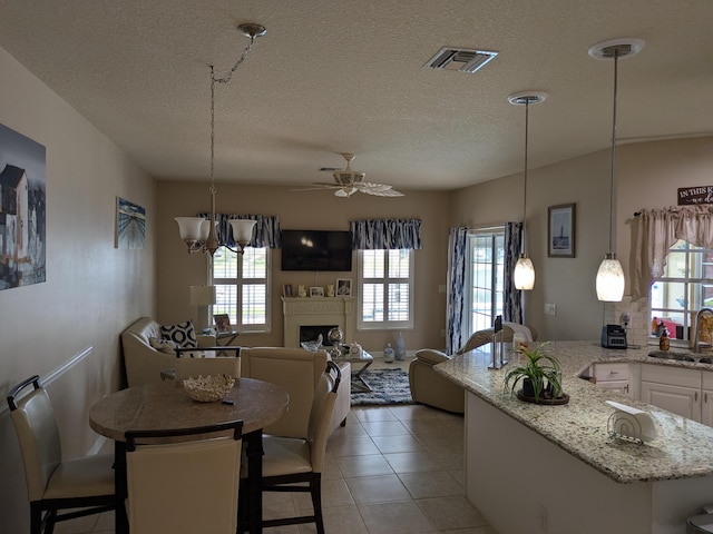 dining area featuring a textured ceiling, tile patterned floors, sink, and ceiling fan with notable chandelier