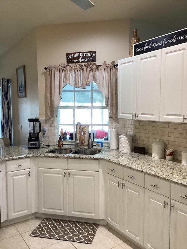 kitchen with white cabinets, light tile patterned flooring, light stone countertops, and sink