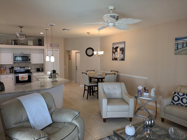 tiled living room with ceiling fan with notable chandelier