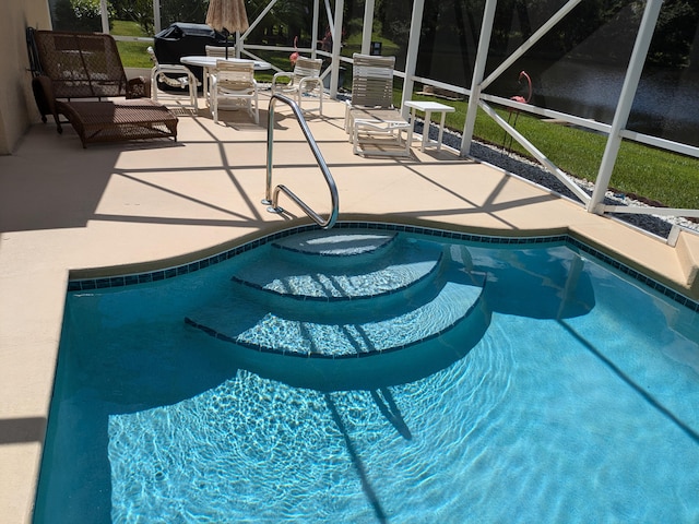 view of pool with glass enclosure, a patio area, and a water view