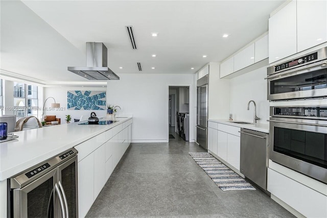 kitchen featuring wall chimney range hood, independent washer and dryer, stainless steel appliances, sink, and white cabinets