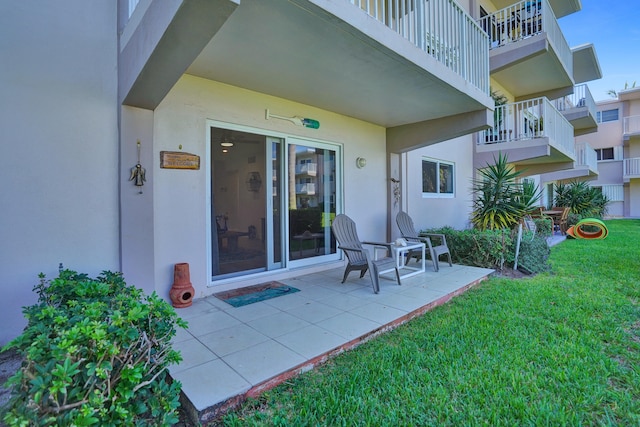 entrance to property featuring a balcony, a patio, and a yard