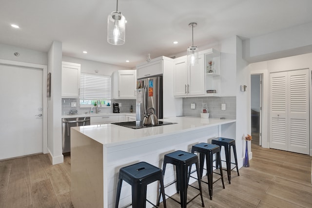 kitchen with white cabinetry, kitchen peninsula, light hardwood / wood-style flooring, stainless steel appliances, and decorative light fixtures