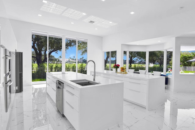 kitchen featuring a center island with sink, sink, stainless steel oven, and white cabinetry