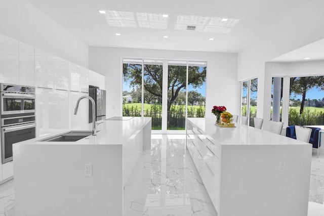 kitchen with a center island with sink, a wealth of natural light, sink, and white cabinets