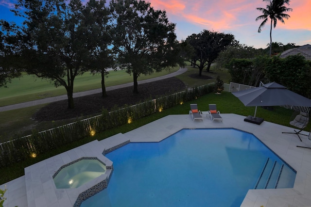 pool at dusk with an in ground hot tub, a patio area, and a lawn