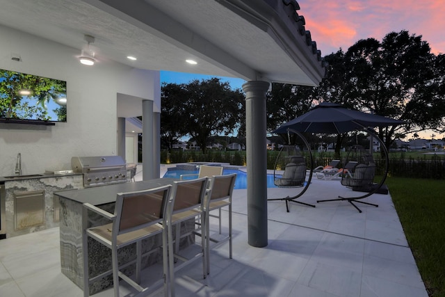 patio terrace at dusk featuring area for grilling and an outdoor kitchen